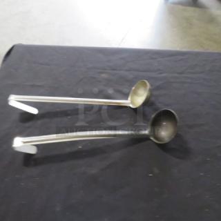 2oz stainless steel ladle set on a dark surface. Long handles, slight wear. Ideal for kitchen or catering use.