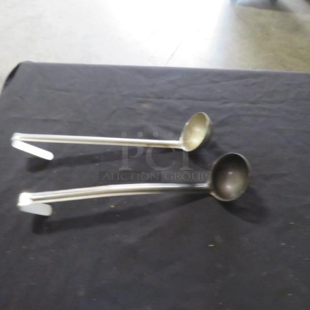 Two stainless steel ladles, 2oz capacity, shown on a black surface. Long handles with hooks, in good condition.