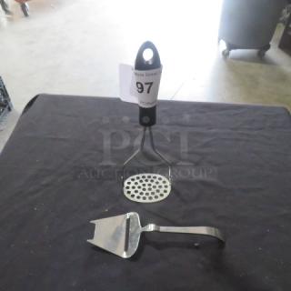 Masher and cheese slicer on display. Masher has a black handle and metal head. Cheese slicer is stainless steel. Both in good condition.