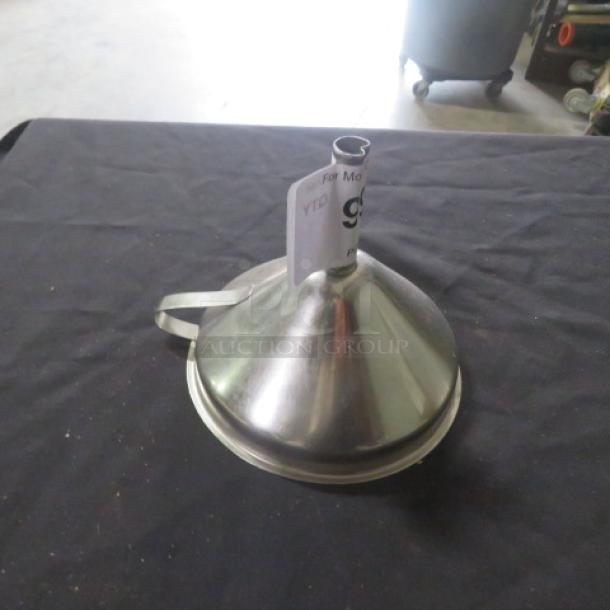 Stainless steel funnel with a handle on a black surface. Includes a paper tag attached to the spout. Good condition.