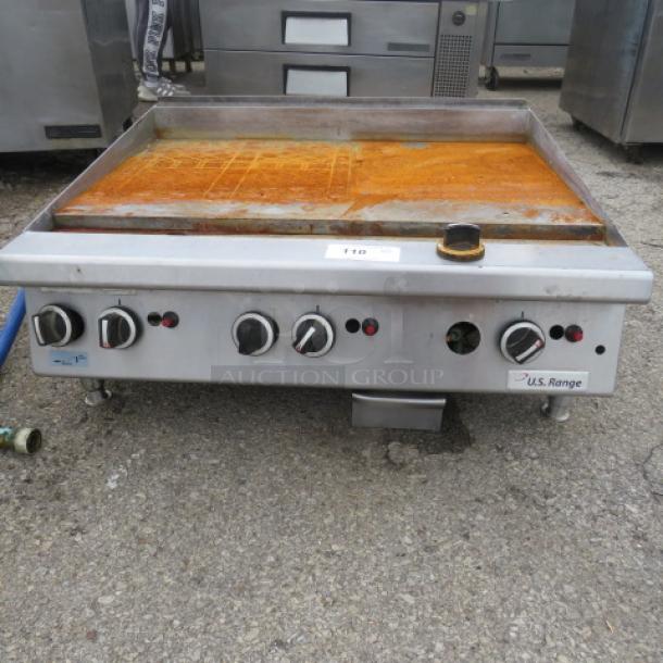 US Range natural gas griddle, 35x32x17 inches. Features four control knobs, stainless steel build, slightly rusted surface.