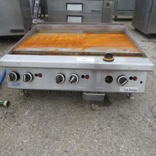 US Range natural gas griddle, 35x32x17 inches. Features four control knobs, stainless steel build, slightly rusted surface.