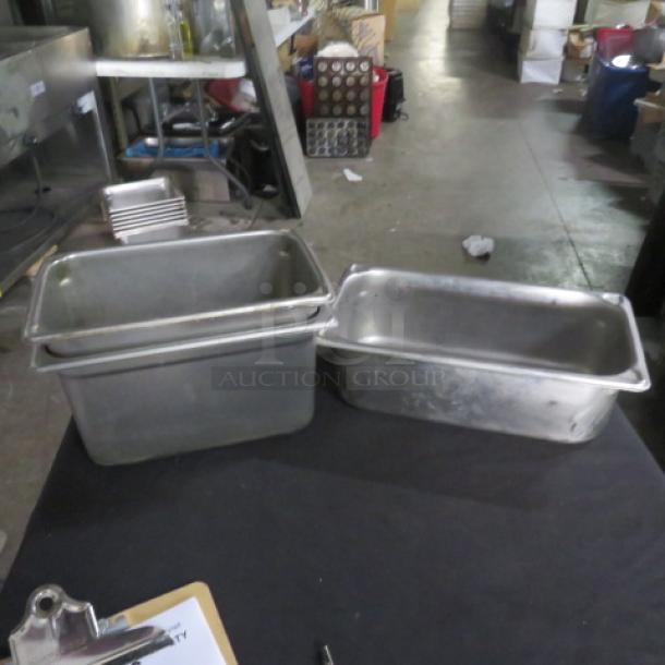 Assorted hotel pans on table; stainless steel; various sizes; used condition; ideal for commercial kitchens.