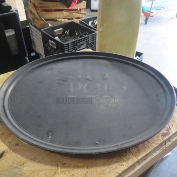 Black 27-inch waitress tray, circular with raised edges, used condition, minor scuffs visible, ideal for restaurant service.