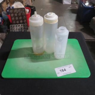 Three plastic squeeze bottles on a green mat, in a lot labeled 164. Bottles show signs of use with some staining.