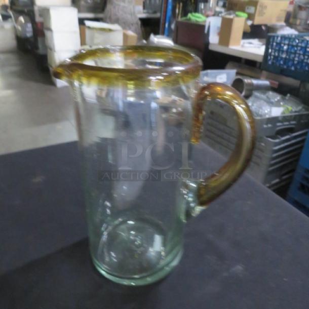 Transparent glass pitcher with amber rim and handle, new condition.