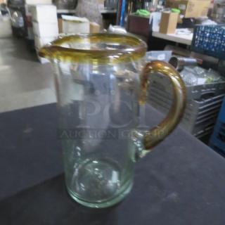 Clear glass pitcher with amber handle and rim, new condition, suitable for beverages or decorative use.