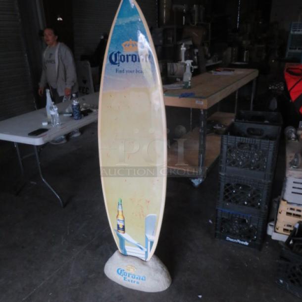 Corona surfboard with branded graphics, standing on a Corona rock holder. Used, good condition, vibrant colors.