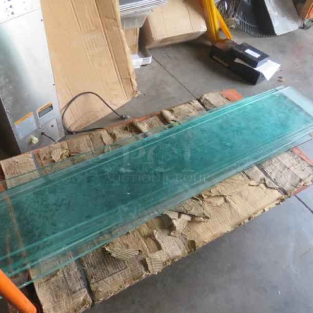 51.5x10 glass shelf, transparent, in good condition, resting on cardboard packaging in a warehouse setting.