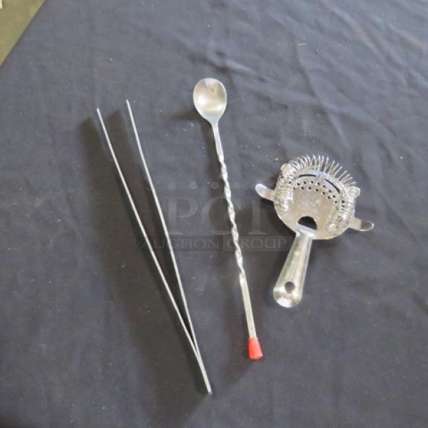 Assorted bar utensils including a twisted stirring spoon, metal tweezers, and a cocktail strainer with coil.