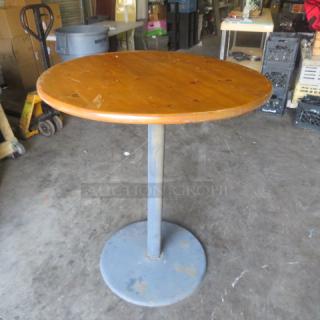 Wooden table top on bar height metal pedestal base, 36x42 inches. Shows moderate wear, suitable for casual settings.