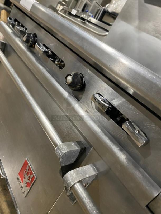 Wolf stainless steel commercial range with 6 burners, griddle, double oven, and broiler. Features knobs and logo.