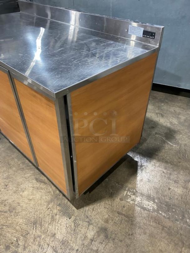 Duke RBC60M bar back refrigerator with stainless steel top, wood-style finish, two doors, upturned backsplash, and legs.