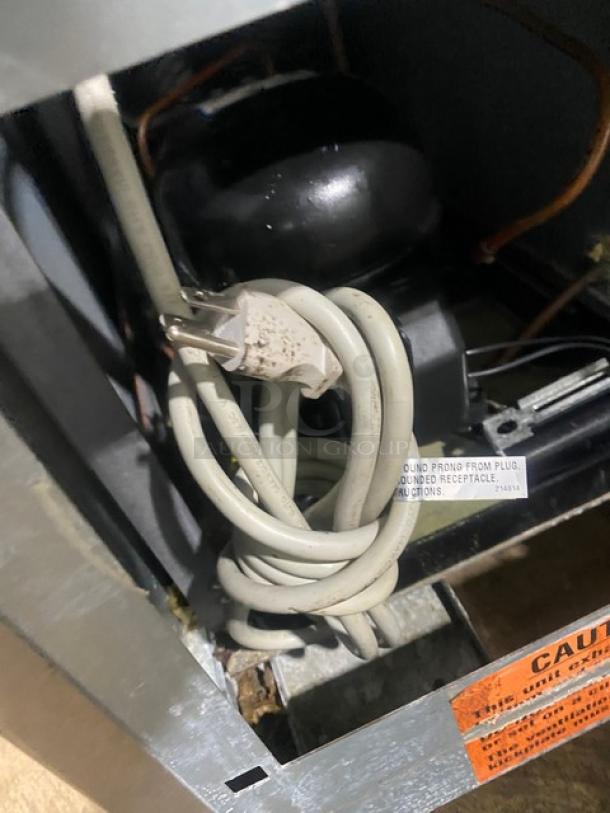 Duke RBC60M bar back refrigerator, stainless steel, wooden style, 2-door, upturned backsplash, visible power cord and caution label.