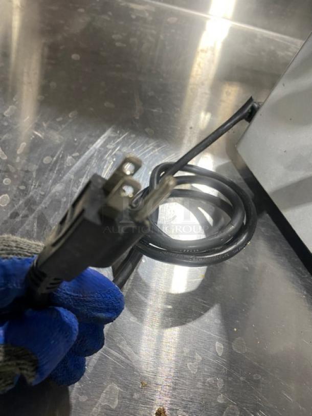 Electric powered countertop deli meat slicer plug and cord, shown on a metal surface, indicating functionality.