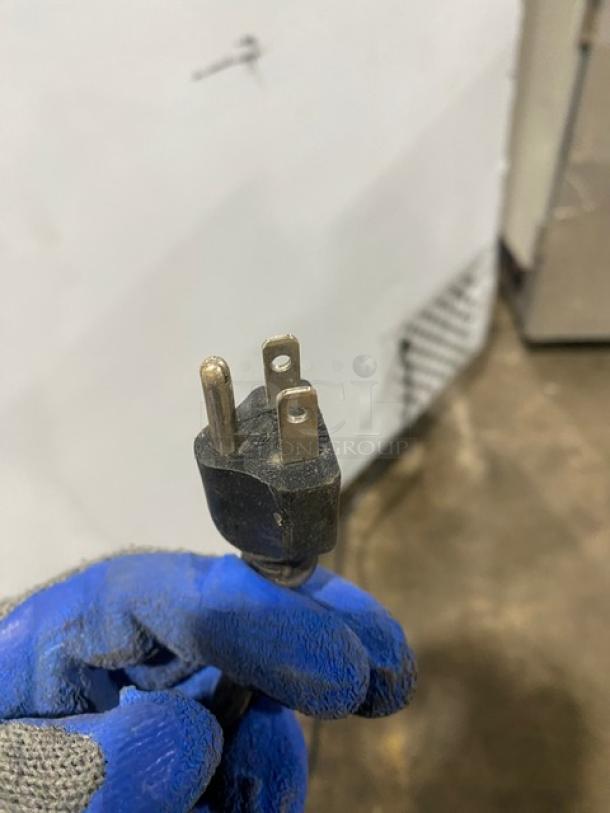 Close-up of a three-prong plug of Leader LB48SC refrigerator. Blue-gloved hand holding plug. Auction detail focus.