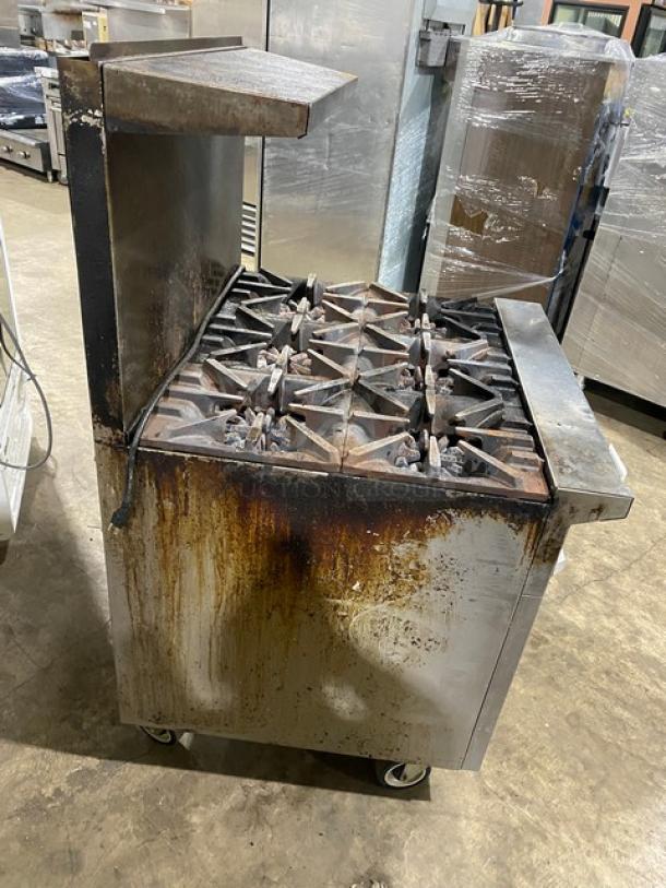 Garland commercial stainless steel gas range with 6 burners, backsplash, overhead salamander shelf, and wired oven rack. On casters. Used condition.