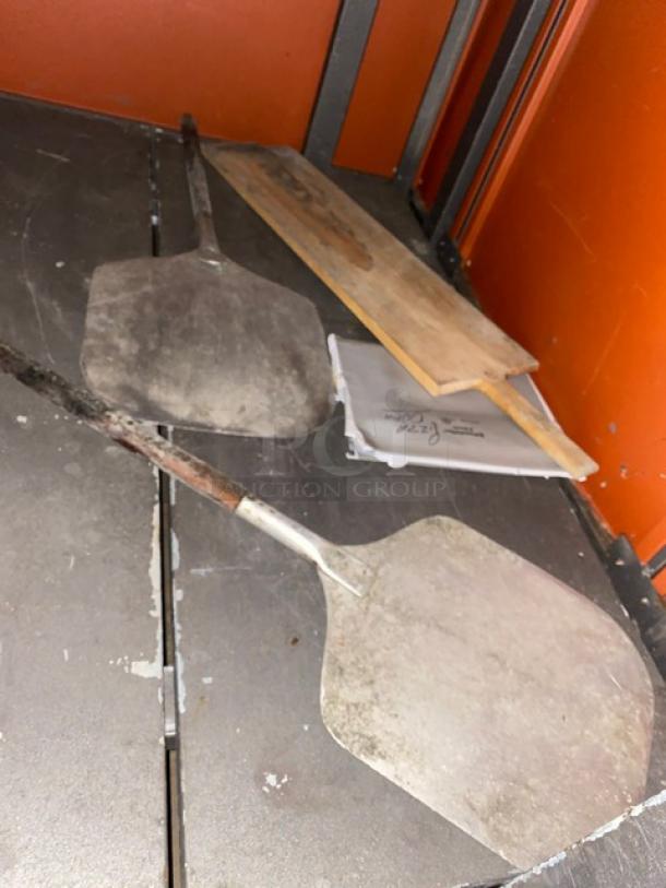 Two metal pizza paddles with wooden handles, part of Izzo Forni commercial electric pizza oven set. Signs of use visible.