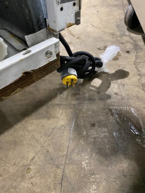 Beverage-Air BRT68P power cord on floor, yellow plug. Partial view of ice cream cabinet base with minor wear.