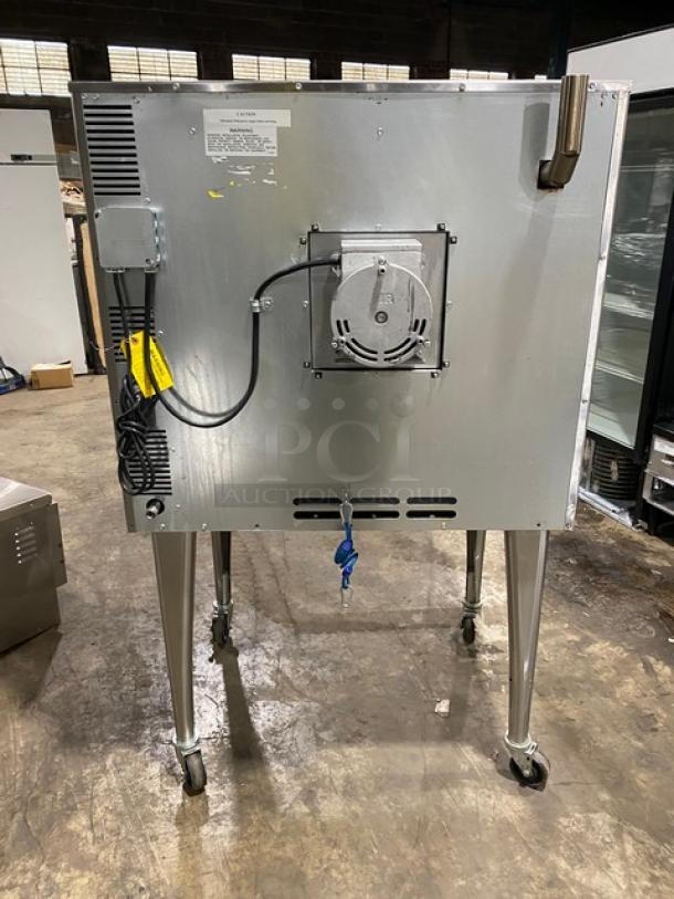 Imperial stainless steel gas convection oven on casters, with wired oven rack, rear view. Features vent and power cords.