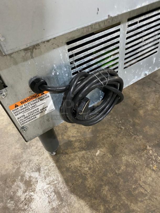 Manitowoc UD0140A commercial ice machine, stainless steel, electric, with undercounter bin, on legs, visible warning label.