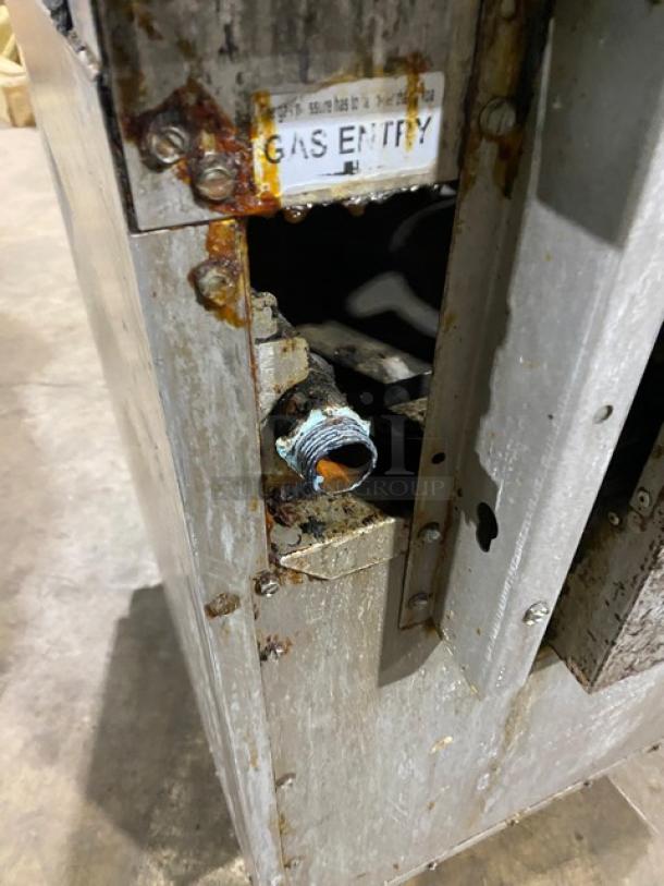 CPG Commercial stainless steel 4-burner range/oven combo with backsplash, overhead salamander shelf, and gas entry labeling. Condition shows rust.