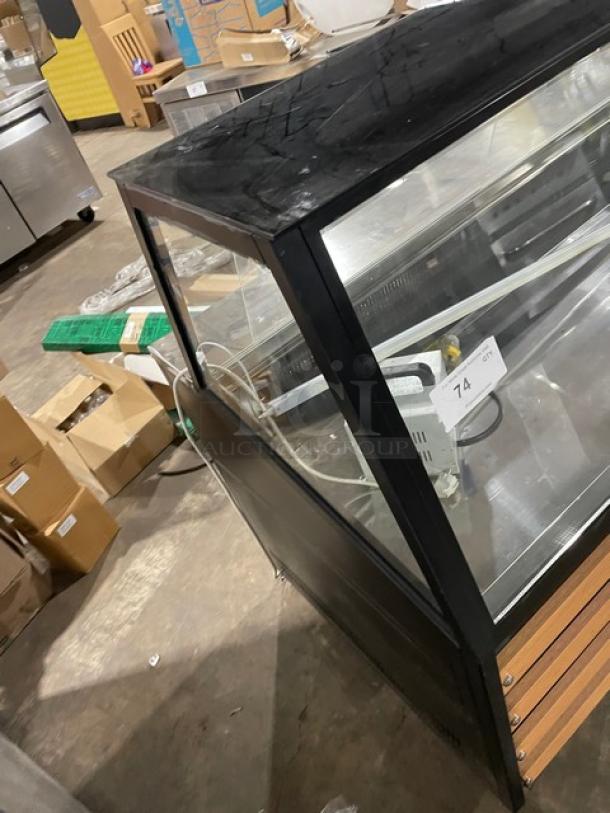 Commercial black slanted glass refrigerated display case on casters with rear prep, lower storage, and double sliding doors.