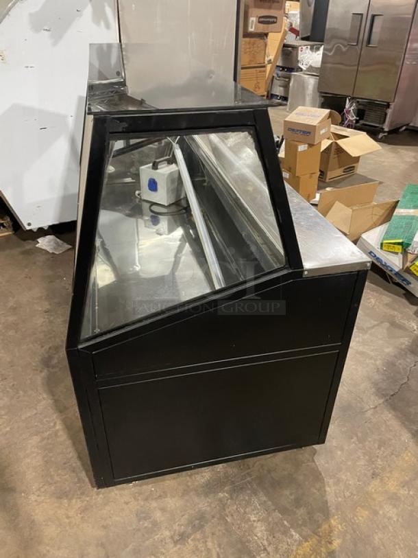 Commercial black slanted glass refrigerated bakery/deli merchandiser display case with rear prep area, lower storage, double sliding doors, and casters.