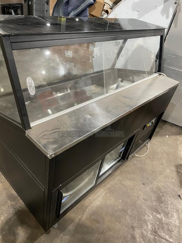 Commercial black refrigerated display case with slanted glass, rear prep area, lower storage, sliding doors, and casters.