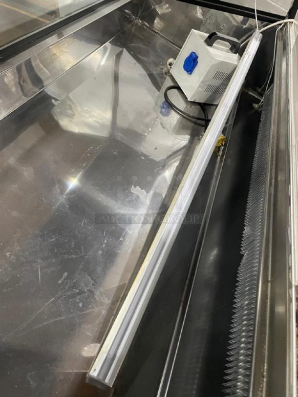 Commercial black slanted glass refrigerated display case with rear prep area, lower storage, sliding doors, on casters.