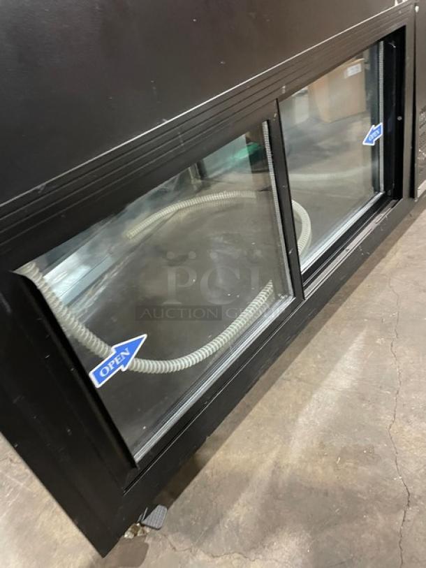 Commercial black slanted glass refrigerated display case, rear prep area, lower storage, double sliding doors, on casters.