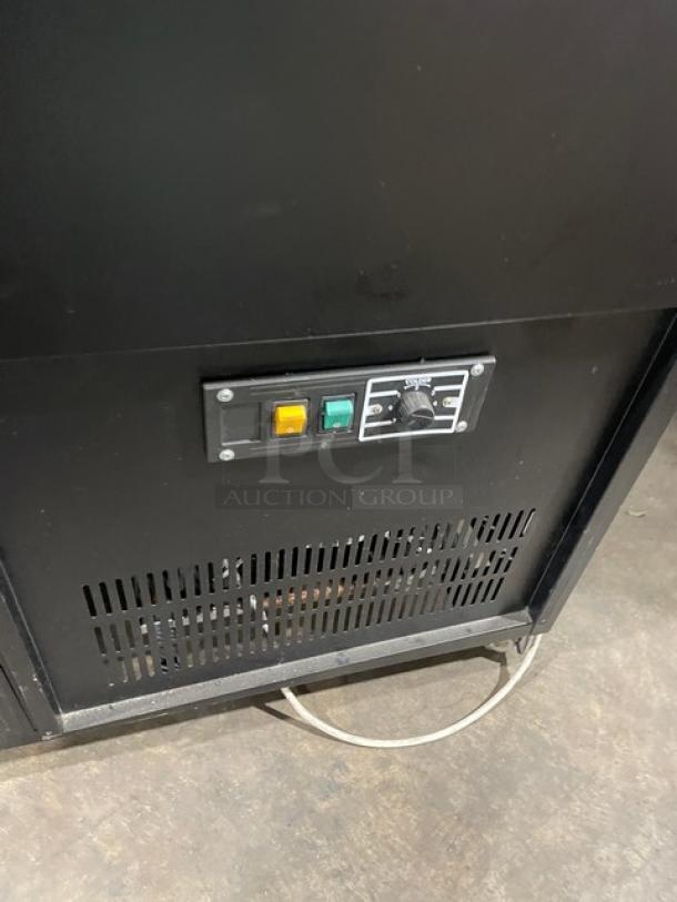 Commercial black slanted glass refrigerated display case with rear prep area, lower storage, double sliding doors, on casters.