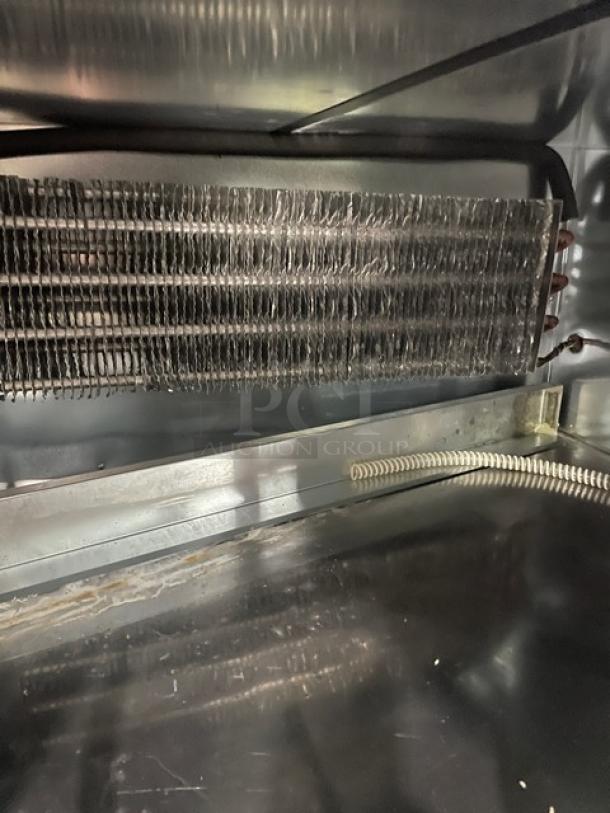 Commercial refrigerated display case interior with cooling coils, metal surfaces, and visible wiring.