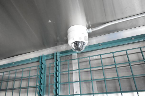 Interior view of a food trailer with stainless steel walls, teal shelving, and a mounted security camera.