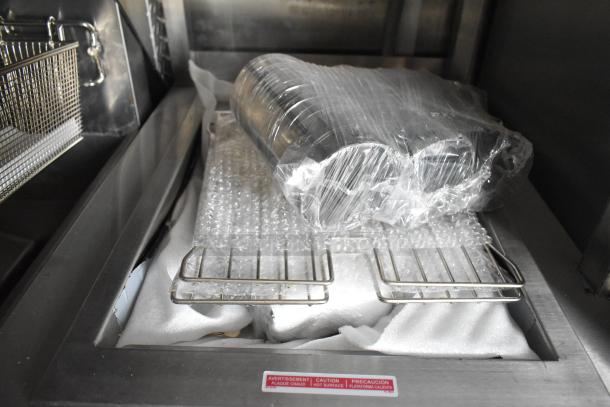 Food trailer interior with packaged stainless steel equipment on metal racks. Hot surface warning label visible.