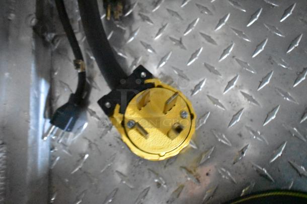 Yellow heavy-duty power plug on diamond plate metal flooring in a food trailer.
