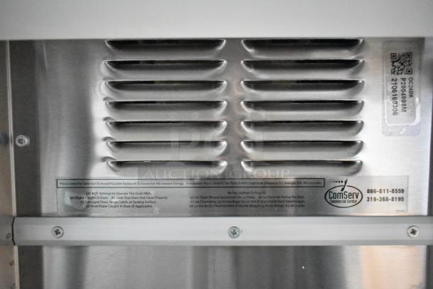 Stainless steel vent with ComServ label, contact info, and microwave safety instructions on a food trailer appliance.