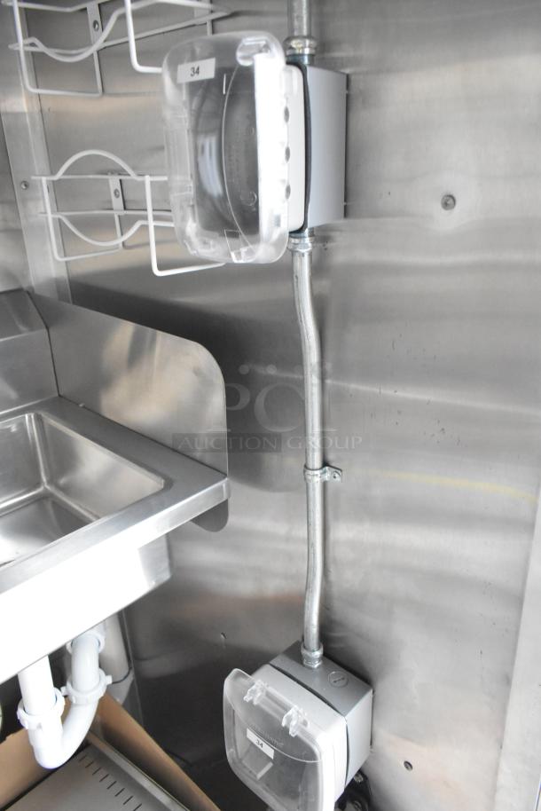 Inside of a food trailer showing stainless steel sink, electrical boxes with clear covers labeled "34".