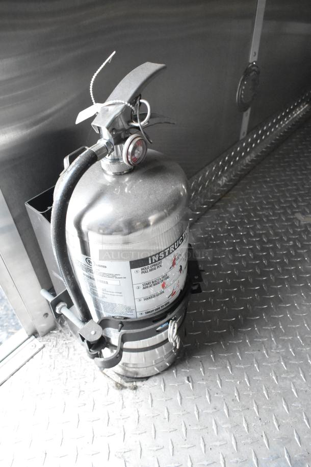 Fire extinguisher mounted inside a food trailer with visible instructions and UL listing, on a metal floor.