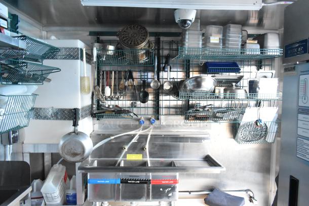 Fully outfitted mobile kitchen trailer interior with commercial-grade appliances, metal shelving, sinks, and utensils. New condition.