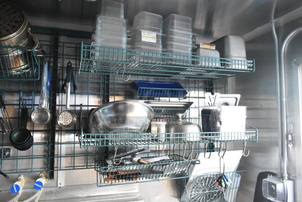 Fully equipped 2021 food trailer kitchen, featuring commercial-grade equipment, racks with utensils, and storage bins.