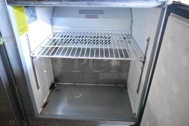Interior view of a commercial-grade cooler inside a food trailer. Features include stainless steel shelving and visible labels on the inside wall. Trailer is brand new, equipped with appliances like True freezers and CaptiveAire hood.