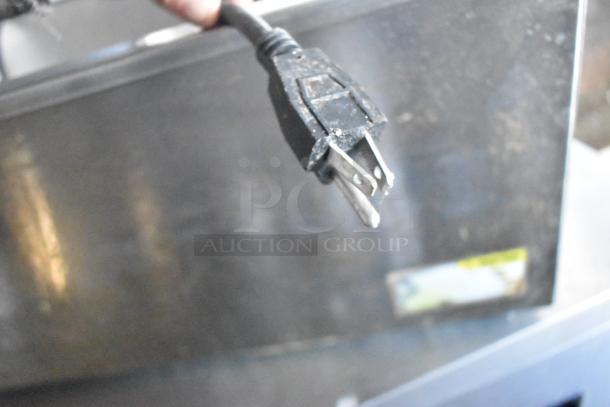 Close-up of a power plug attached to a commercial-grade kitchen appliance. Background shows part of a metallic unit.