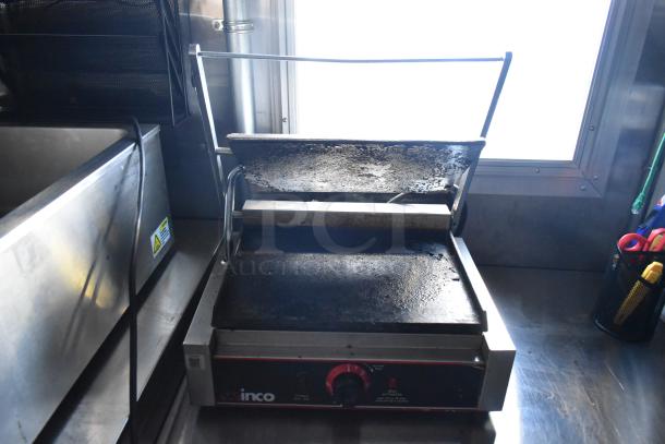 Winco commercial panini press in food trailer. Used condition, stainless steel body, adjustable heat settings, visible grease buildup.