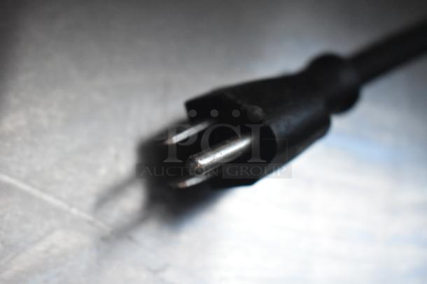 Close-up of a black electrical plug on a metallic surface, showing two exposed prongs.