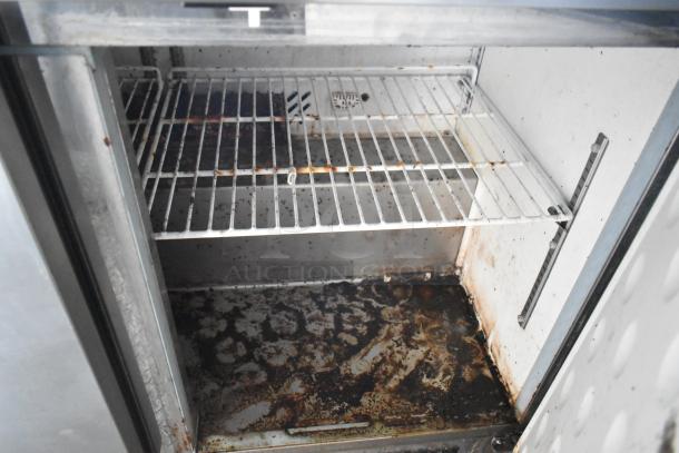 Interior of used commercial freezer with wire shelving and visible rust and grime on the floor.