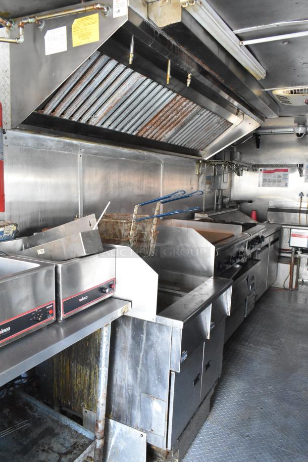 Fully equipped food trailer kitchen with Pyrochem grease hood, gas fryer, Arctic Air coolers, prep tables, and Wells range.