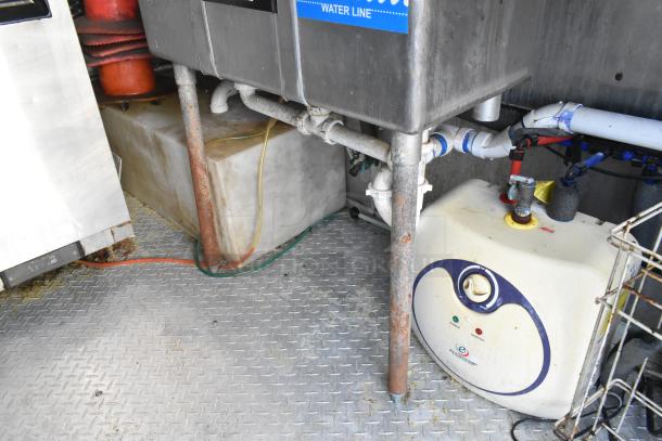 Commercial-grade food trailer interior showing plumbing system beneath stainless sinks and various pipes, in new condition.