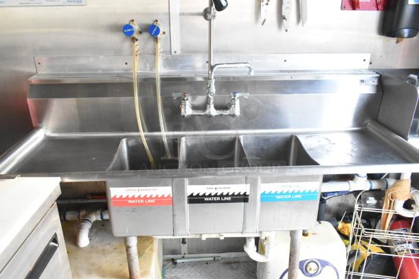 Commercial-grade sink setup with three labeled compartments for sanitizing, rinsing, and washing in a food trailer kitchen.