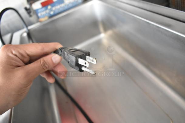 Close-up of a hand holding a power plug inside a new food trailer's stainless steel sink.